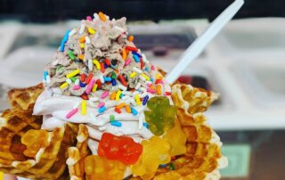 Ice cream with gummy bears and sprinkles served in a waffle bowl